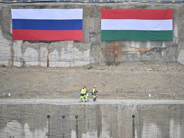 Magyar és orosz nemzeti zászlók egy falon, miközben munkások sétálnak a Paks II. építkezésén  2026. február 5-én