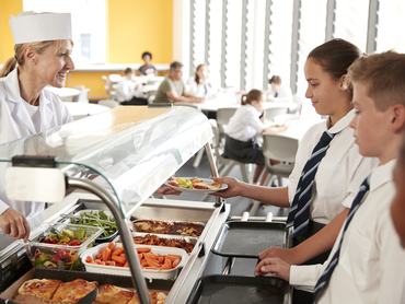 High School Students Wearing Uniform Being Served Food In Canteen