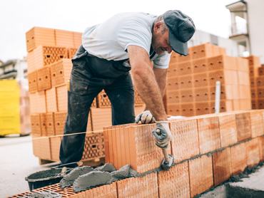 industrial worker building exterior walls, using hammer for laying bricks in cement. Detail of worker with tools and concrete