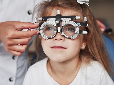 Health care of the eyes. Doctor checking little girl sight and tuning the phoropter.