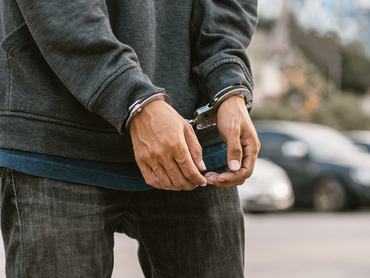 Under arrest, a man's hands with clenched fists are handcuffed behind him. Black background with copy space.