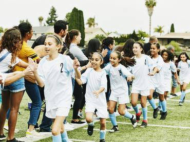 Young female soccer team giving high fives to parents on sidelines after game