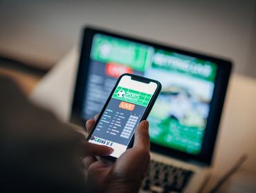 Mature man using mobile app for live betting and online gambling and watching a sports match