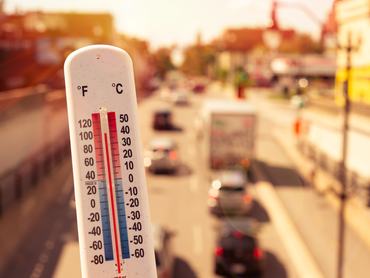 Thermometer in front of cars and traffic during heatwave in Montreal.