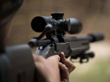 Sniper shooting rifle by looking through a scope.