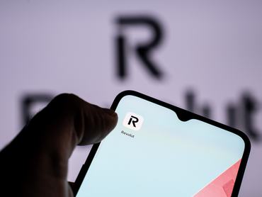 A person is holding a mobile phone with the Revolut application in front of a screen displaying the Revolut logo. (Photo by Nikos Pekiaridis/NurPhoto via Getty Images)