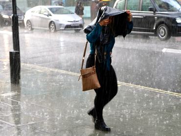 London, UK. August 7th 2021.  Woman walking down Oxford Street in a heavy summer rain shower.