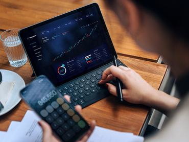 Young Asian businesswoman managing personal finance and investment. Checking investment and stock market trades, making financial plans and setting financial goals with smartphone and digital tablet in cafe. Wealth management and online banking