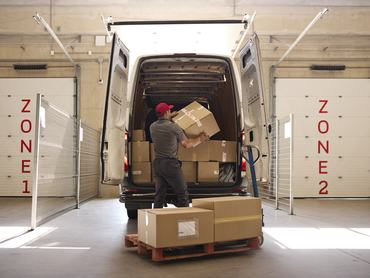 Warehouse worker loading packaged cardboard boxes in van at warehouse dock