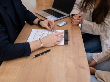Financial advisor engaging with clients during an office meeting, discussing investment strategies while utilizing documents and a laptop for effective communication and planning