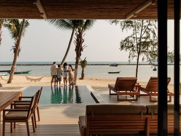 A joyful family shares a warm embrace beside the pool in their villa’s, gazing at the beautiful view of the beach and the sparkling sea in the background, in Koh Phangan, in Thailand.