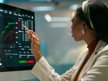 Woman, computer screen and trading charts at office, point and review for growth with profit at agency. African person, investor and monitor for stats, portfolio and graphs with fintech at company