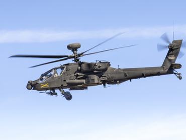 The image shows an AH-64 Apache attack helicopter performing at the Bremerton Air Show. The aircraft is operated by the U.S. Army. The insignia of the crossed swords on the side of the fuselage represents the 7th Cavalry. The photo was taken in July 2025 at the Bremerton Airport, Washington, USA