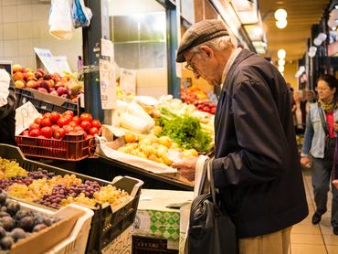 Budapest, Hungary - October 30, 2013: Senior Gentleman shopping for fruit and veg, holding shopping bag and money. Also a female shopper can be seen in the picture.Taken at the great market hall in Budapest, Hungary.