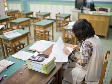 Female teacher is marking exam papers in classroom