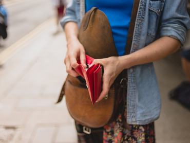 A young woman is standing in the street and is opening her purse to make a purchase