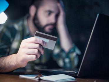 Close-up of a man paying bills from home by using a laptop and a credit card