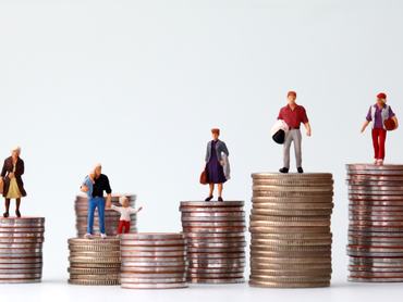 Miniature people standing on piles of different heights of coins. The concepts of person and wealth.