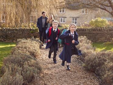 Parents Returning Home From School With Children Wearing School Uniform Running Down Path