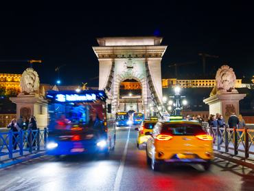 Budapest, Hungary - November 7, 2025: Iconic Chain Bridge at night in Budapest with motion blurred bus and cars passing by the stone lion statue.