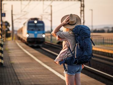 Woman backpacker with hat standing at railroad station and looking to arriving train