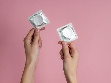 Female hands holding condom on pink background. Top view. The concept of sexual preservation