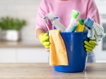 View of a bucket full of cleaning products being held by a woman wearing rubber gloves